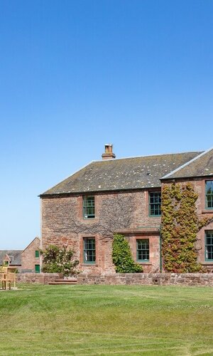 The Farmhouse new addition to The Edinburgh Address - Traditional brick farmhouse on open land with a blue sky.