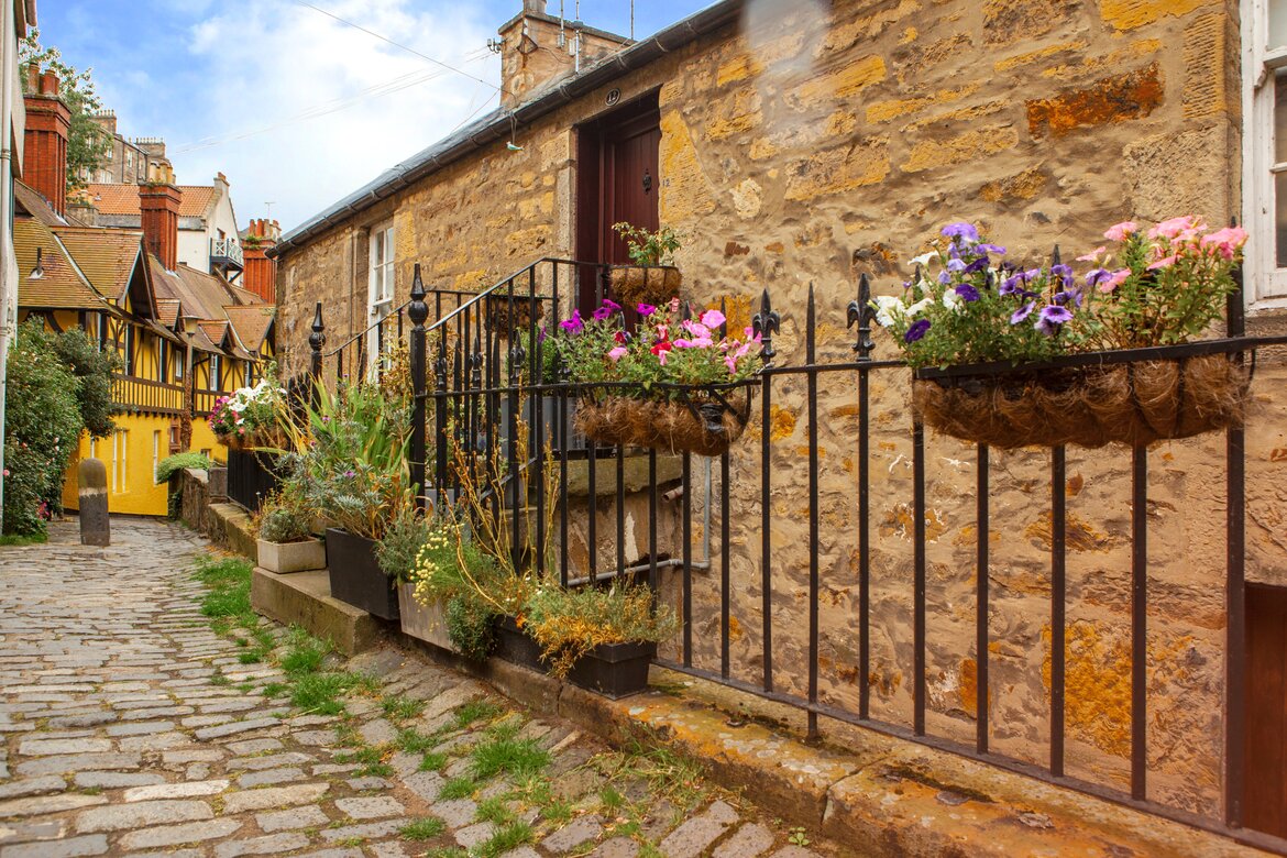 Should I visit Dean Village in Edinburgh?? - A cobbled road lined with iron fencing holding wrought iron flowering hanging baskets.