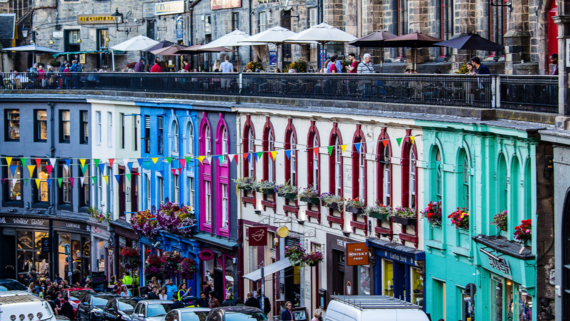 Visit Victoria Street on your stay in Edinburgh - Colourfully painted buildings line the street with people walking alongside.