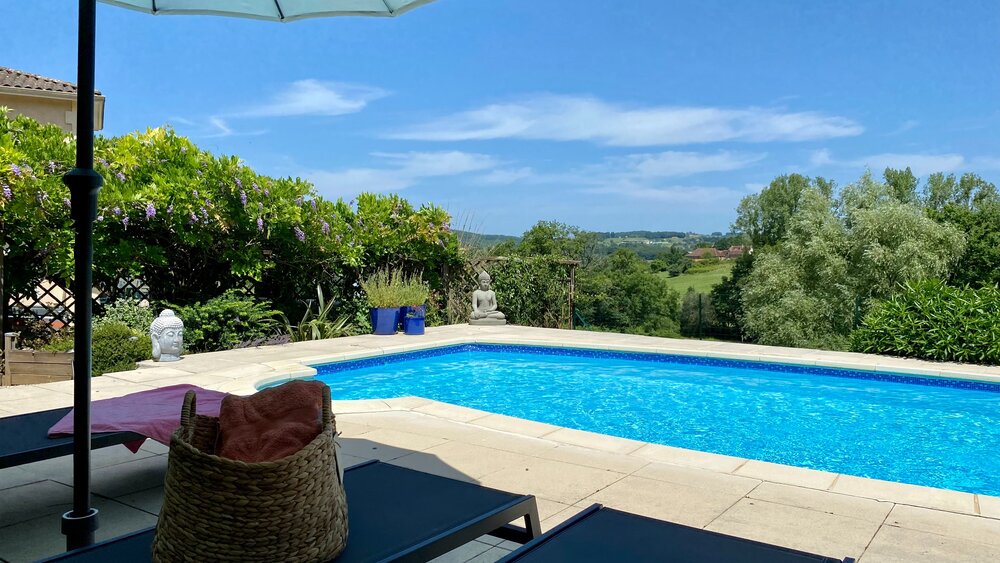 Villa de la Colline en Dordogne - Photographie au bord de la piscine&nbsp;: piscine bleue, collines verdoyantes en arrière-plan. Transats et parasols. (© Voila Villas France)