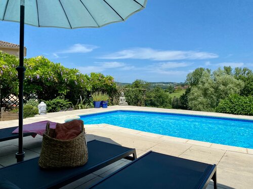 Villa de la Colline en Dordogne - Photographie au bord de la piscine : piscine bleue, collines verdoyantes en arrière-plan. Transats et parasols. (© Voila Villas France)