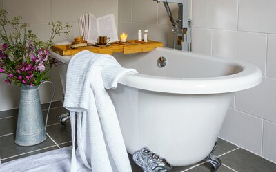 Bathroom by Room in a Private Residential Tenancy - Close up of a white standalone bath with silver feet, in a bathroom with decorative details and floral décor
