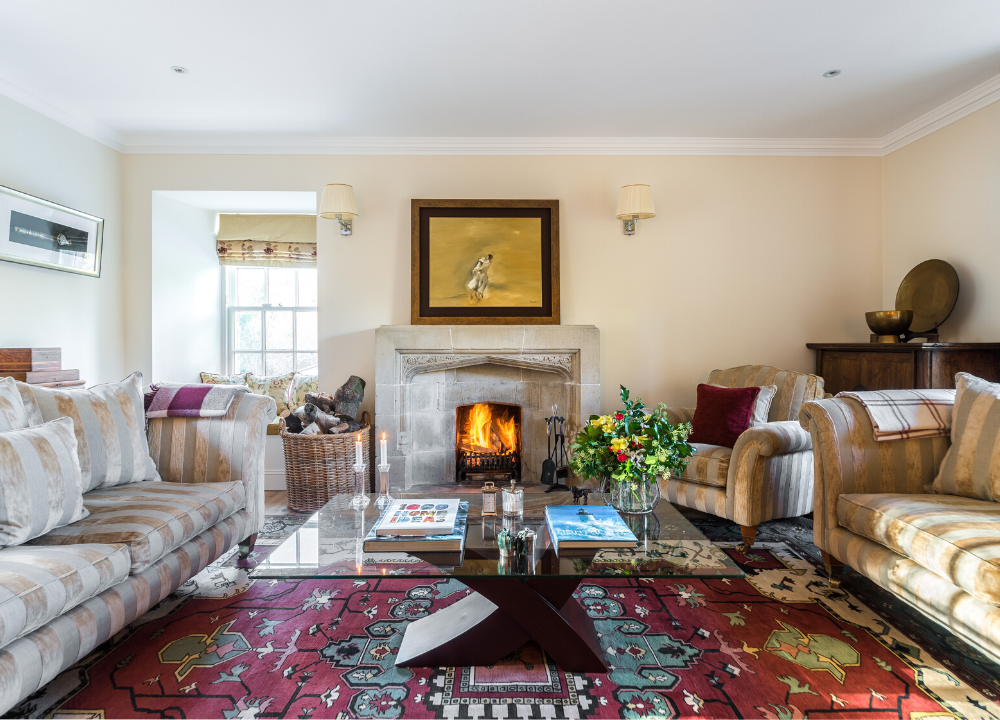 Living room with fireplace of The Riverside House - Ample living space with a red rug, a lit fire and light sofas.