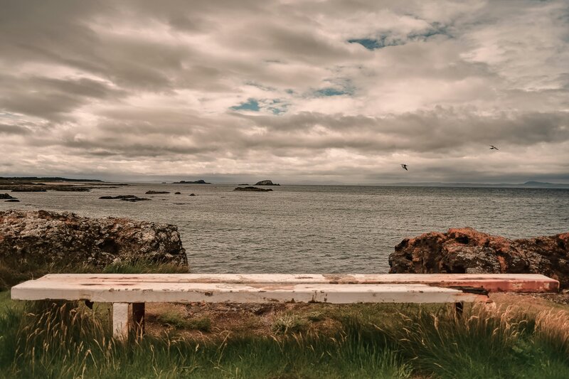 North Berwick bench - Serene view of North Berwick's rugged coastline with a rustic bench and dramatic sky (© 2020 Michael Porter) North Berwick bench - Serene view of North Berwick's rugged coastline with a rustic bench and dramatic sky (© 2020 Michael Porter)