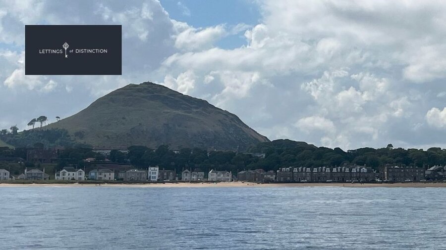 Climb North Berwick Law - A view from a boat of a pointed tall hill behind a coastline.