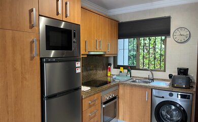 Kitchen - A well-equipped kitchen featuring light wood cabinetry, a stainless steel refrigerator with an integrated microwave, and an under-counter washing machine. (© Goto Property Management)