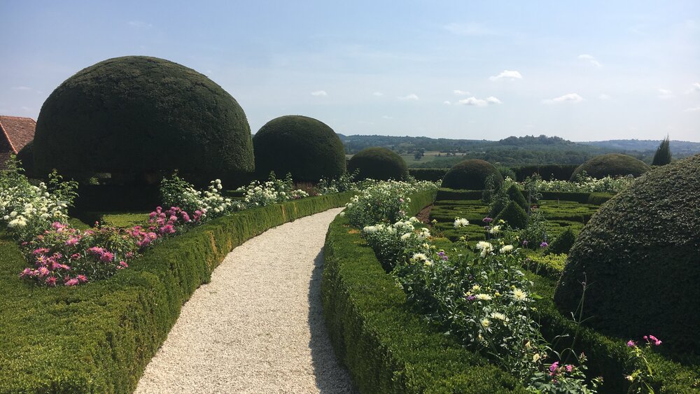 Château de Hautefort - Haies topiaires avec allée de gravier et fleurs blanches dans les jardins du château de Hautefort (© Voila Villas France)