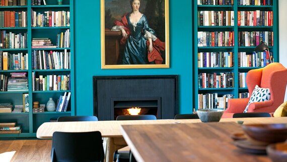 1064305-secret-walled-garden-north-berwick-4 - Bookshelves lining a turqouise wall with lit fire. (© Secret Walled Garden)