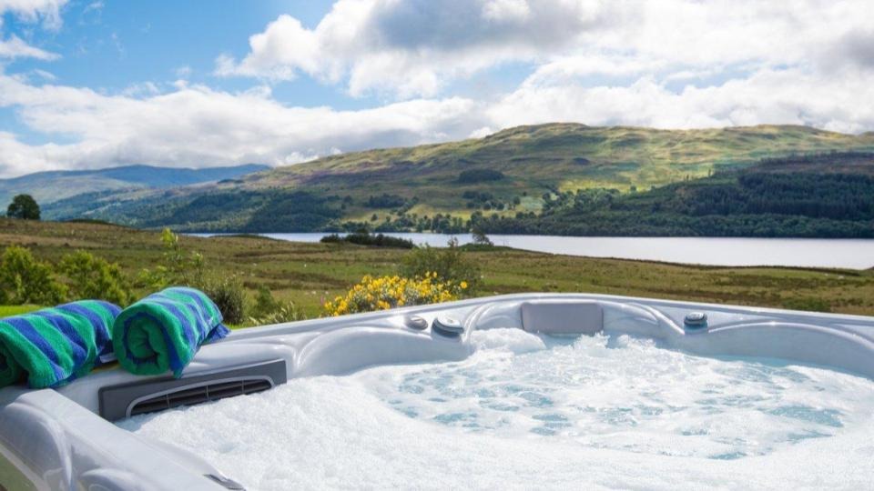 Hot tub in a luxury holiday home in Scotland - View from a bubbling hot tub, over a river and the hills in the distance, under blue skies with some clouds.