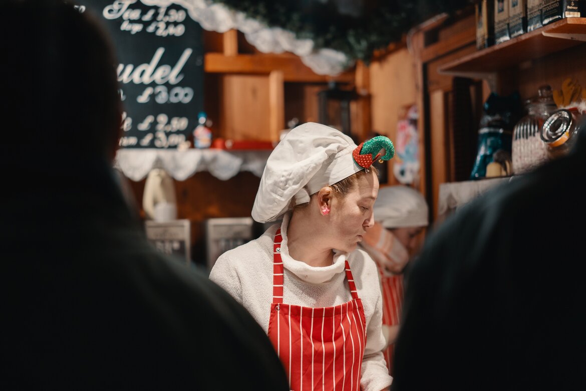 Enjoy the Edinburgh Christmas market - A lady in a red apron working at a Christmas stall. (© Ross Sneddon)