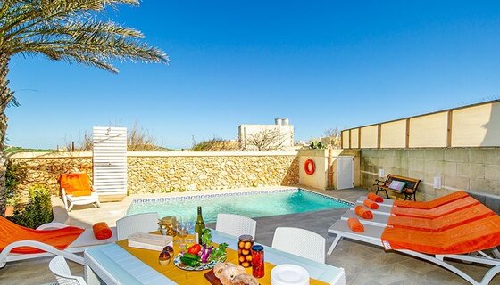 2 bedroom holiday villa in Gozo - Photo of a dining table in front of an open air pool with blue skies. (© Dar It-Torri) 2 bedroom holiday villa in Gozo - Photo of a dining table in front of an open air pool with blue skies. (© Dar It-Torri)