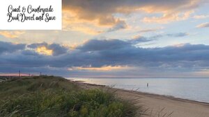 Beach views from Norfolk Coast and Countryside - Sunset shining through dark clouds over a beach with golden sands, and green plants.