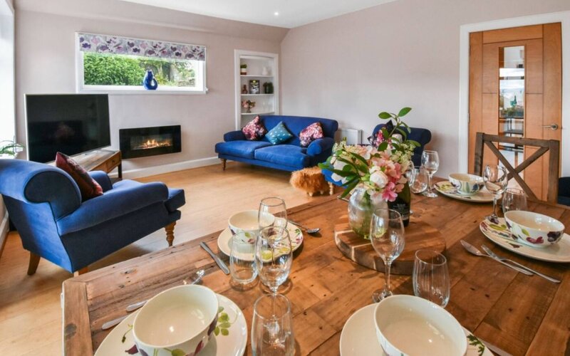 Spacious Living & Dining Room with Serene Garden Views - A bright, inviting living room featuring a comfortable seating area, a wooden dining table, an electric fireplace and delightful garden views