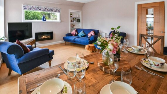 Spacious Living & Dining Room with Serene Garden Views - A bright, inviting living room featuring a comfortable seating area, a wooden dining table, an electric fireplace and delightful garden views