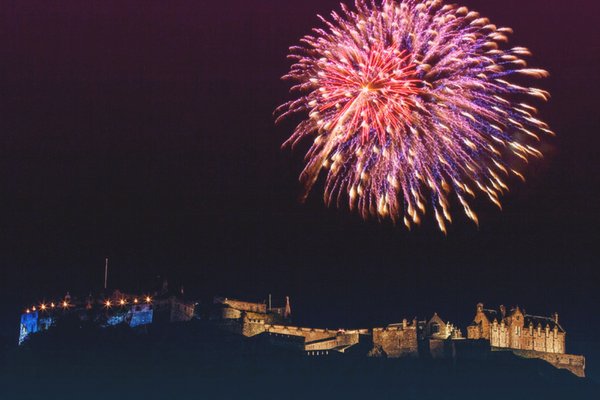 Fireworks above Edinburgh castle in December - Red and pink firework explosion above the castle at night.