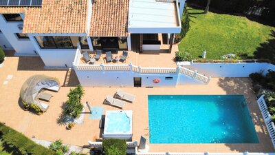 Aerial View of Villa Garden - An aerial perspective captures a private garden with a swimming pool, a hot tub, sun loungers, and a shaded outdoor seating area. The terrace features a mix of tiled flooring and lawned garden space with mature plants. (© Goto Property Management)