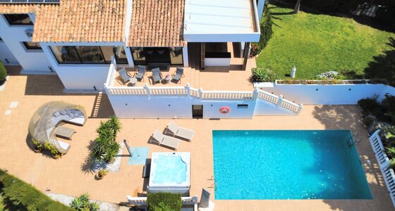 Aerial View of Villa Garden - An aerial perspective captures a private garden with a swimming pool, a hot tub, sun loungers, and a shaded outdoor seating area. The terrace features a mix of tiled flooring and lawned garden space with mature plants. (© Goto Property Management)
