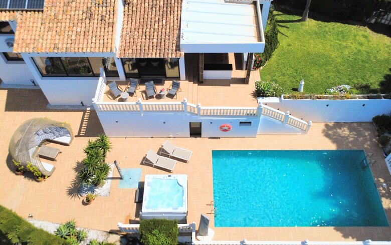 Aerial View of Villa Garden - An aerial perspective captures a private garden with a swimming pool, a hot tub, sun loungers, and a shaded outdoor seating area. The terrace features a mix of tiled flooring and lawned garden space with mature plants. (© Goto Property Management)