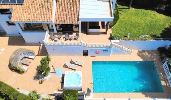 Aerial View of Villa Garden - An aerial perspective captures a private garden with a swimming pool, a hot tub, sun loungers, and a shaded outdoor seating area. The terrace features a mix of tiled flooring and lawned garden space with mature plants. (© Goto Property Management)