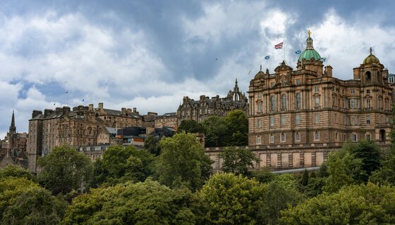 Visit Edinburgh's rich history - A view of grand old buildings set behind parkland with trees and grass. (© Winston Tjia Tu @ Unsplash)