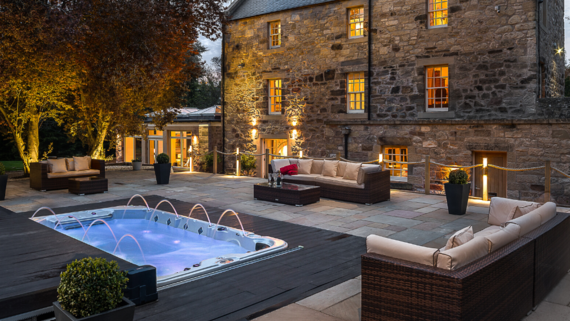 The Riverside House at Dalkeith - Exterior of a large house with hot tub and external seating in the foreground.