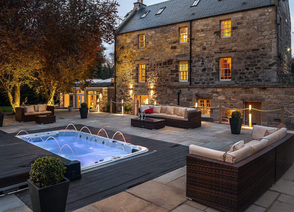 The Riverside House at Dalkeith - Exterior of a large house with hot tub and external seating in the foreground.