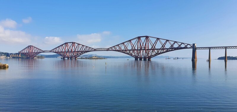 Cycle across the Forth Road bridge to view the Rail bridge - A view of the Forth Rail Bridge and the Firth of Forth river under a blue sky.
