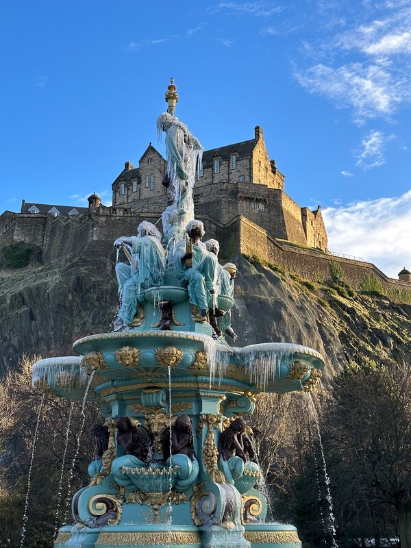 Ross Fountain and Edinburgh Castle - The ornate Ross Fountain stands in the foreground, featuring icy water features with Edinburgh Castle rising prominently on the rocky cliff behind it. (© 2023 Robin Morris)