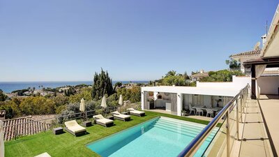 Private Pool with Sea Views - An elevated view of a rectangular swimming pool surrounded by artificial grass and sun loungers, overlooking a coastal landscape. (© Goto Property Management)