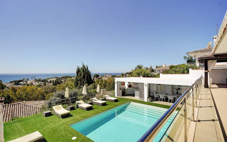 Private Pool with Sea Views - An elevated view of a rectangular swimming pool surrounded by artificial grass and sun loungers, overlooking a coastal landscape. (© Goto Property Management)