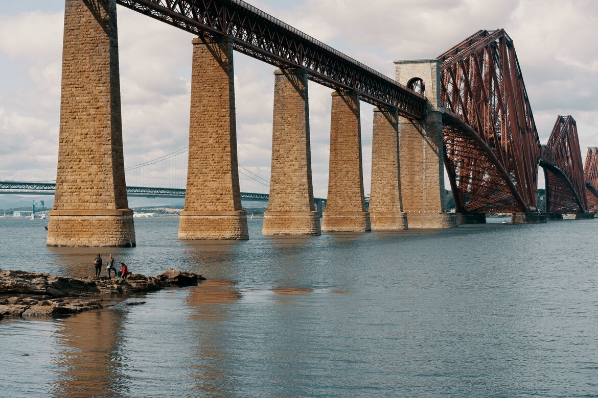 The Forth Bridge in South Queensferry - A majestic red rail bridge spanning a river. (© Ross Sneddon on Unsplash)