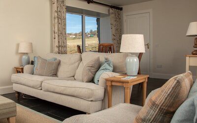 Cosy Lounge with High Speed Internet in Scotland - Well-lit lounge area with sumptuous seating and chic décor, featuring a picture window that frames the tranquil hills of the Isle of Skye