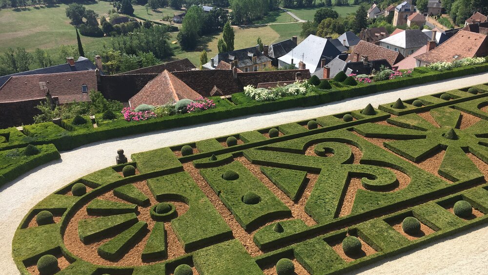 Hautefort Chateau Gardens - Topiary gardens of Hautefort Chateay with the rooftops of the village below and surrounding green rolling countryside of Dordogne. (© Voila Villas France)