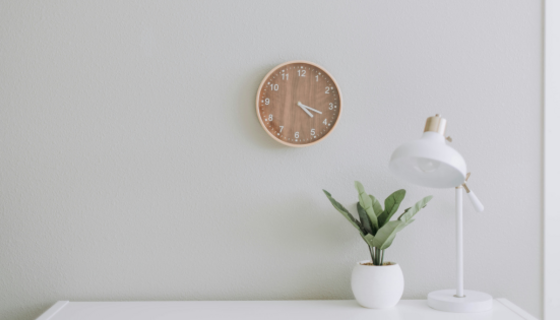 Business accommodation in Scotland - A white scene of a white lamp and plantpot on a white desk, with a simple brown clock. (© Samantha Gades on Unsplash)