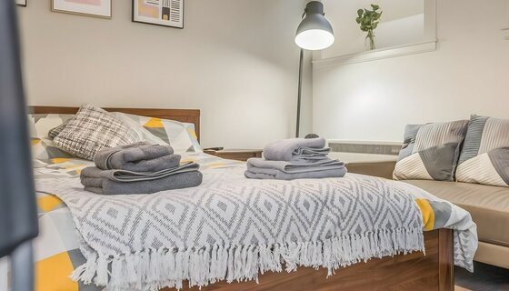 Budget-friendly holiday homes in Scotland - An airy room with a double bed covered with a light blanket, a sofa, and a tall lamp in the corner. (© The Bristo Residence)