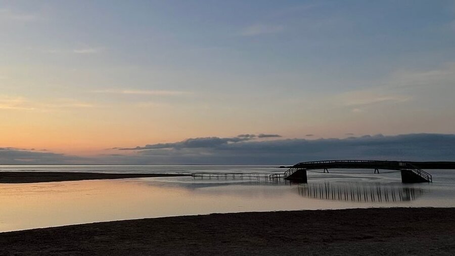 Belhaven Bridge at Belhaven Bay - A bridge sits stranded, casting reflection into the surrounding water, with the sunset in the background.