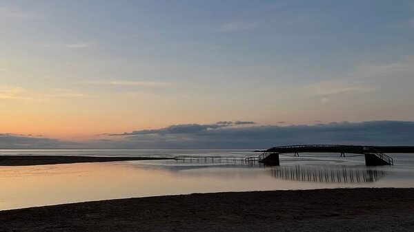 Belhaven Bridge at Belhaven Bay - A bridge sits stranded, casting reflection into the surrounding water, with the sunset in the background.
