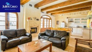 Case Study of Jules Gozo Holidays - A photo from Jules Gozo Holidays, with an open living space comprised of two leather sofas and a wooden coffee table with wooden beams leading to a spacious kitchen.