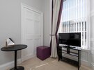 Queen Bedroom Seating and TV Area - Bright bedroom corner featuring a  TV, a small table with a vanity mirror and a purple cube ottoman